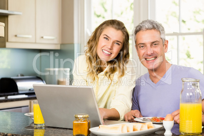 Happy couple using laptop and having breakfast