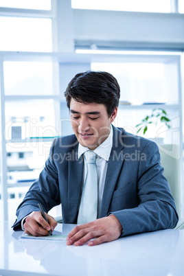 Smiling asian businessman completing a cheque
