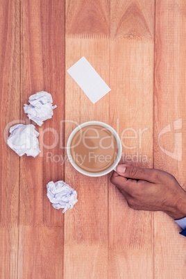 Hand holding coffee cup by paper balls on desk