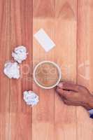 Hand holding coffee cup by paper balls on desk