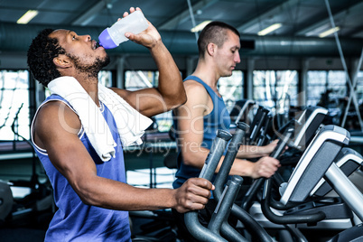 Man drinking water while using elliptical machine