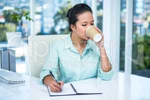 Smiling businesswoman writing notes with a coffee