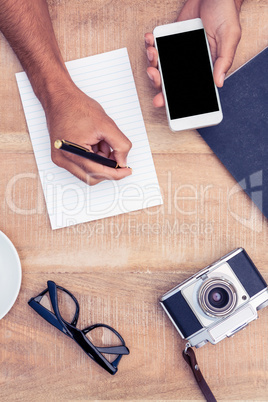 Cropped image of man writing on notepad while holding smart phon