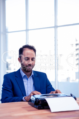 Businessman working on typewriter while sitting at desk in offic
