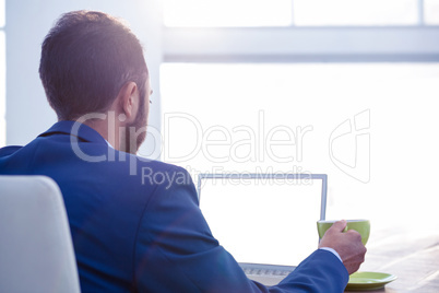Business professional holding coffee cup while working on laptop