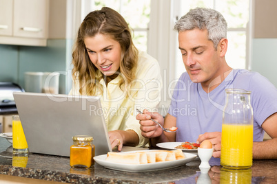 Happy couple using laptop and having breakfast