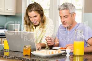 Happy couple using laptop and having breakfast