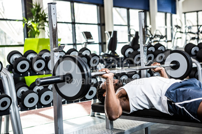 Muscular man lifting barebell while lying on bench