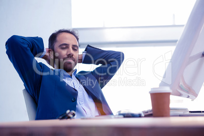 Businessman relaxing with hands behind head in bright office