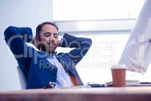 Businessman relaxing with hands behind head in bright office