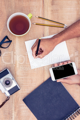 Businessman writing on notepad while holding smart phone