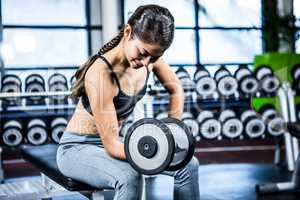 Muscular woman lifting dumbbell while sitting on bench