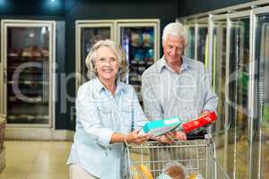 Smiling senior couple with cart buying food