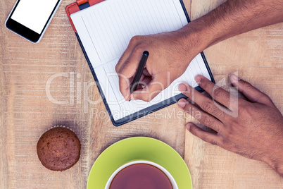 Cropped image of man writing on diary at table