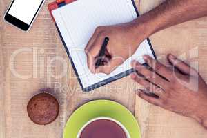 Cropped image of man writing on diary at table