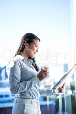 Smiling businesswoman holding disposable cup reading newspaper