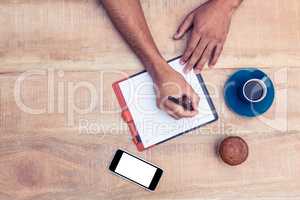 Man writing on diary at table by coffee and cup cake