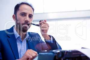 Portrait of businessman using typewriter while holding smoking p