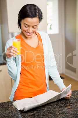 Smiling brunette reading newspaper and holding glass with orange