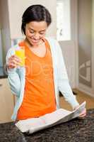 Smiling brunette reading newspaper and holding glass with orange