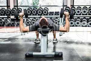 Muscular man lifting dumbbells while lying on bench