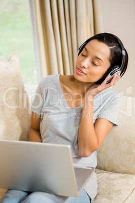 Smiling brunette using laptop and headphones