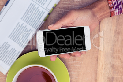 Man using smart phone by coffee and newspaper on table