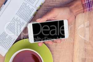 Man using smart phone by coffee and newspaper on table