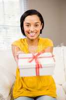 Smiling brunette holding gift to the camera