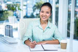 Smiling businesswoman writing notes with a coffee