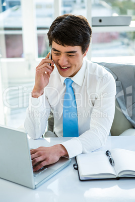 Busy asian businessman working on laptop and calling