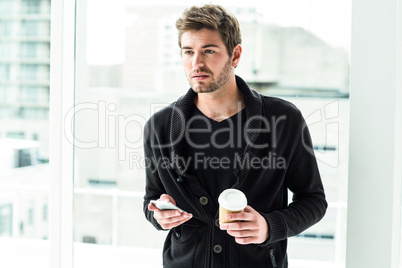 Handsome man holding smartphone and disposable cup