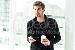 Handsome man holding smartphone and disposable cup