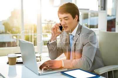 Busy asian businessman working on laptop and calling