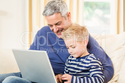 Father and son using laptop on the sofa