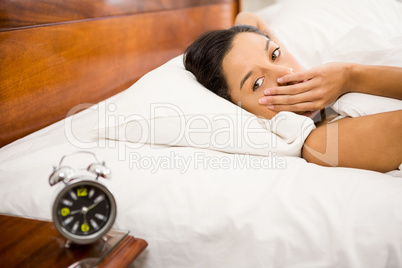 Brunette in the bed looking at alarm clock on the table