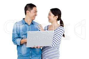 Cheerful couple looking at each other while holding laptop
