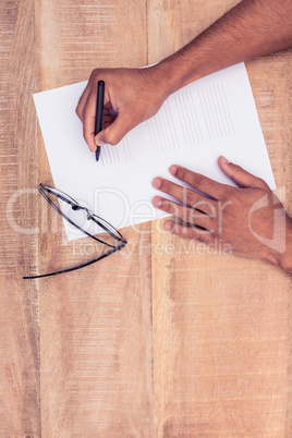 Businessman writing on paper by eye glasses at desk