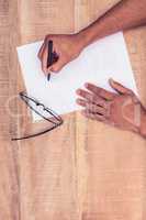 Businessman writing on paper by eye glasses at desk