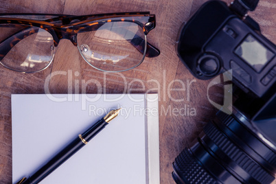 Pen on paper by camera and eye glasses at table