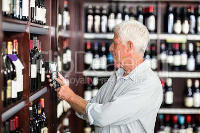 Smiling senior man scanning wine bottles