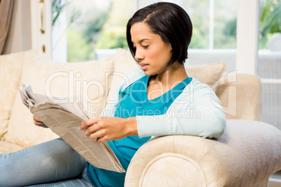 Attractive brunette reading newspaper on the sofa