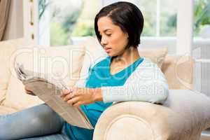 Attractive brunette reading newspaper on the sofa
