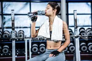 Muscular woman sitting on bench while drinking water