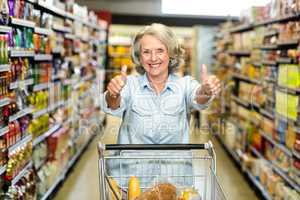 Smiling senior woman with cart showing thumbs up