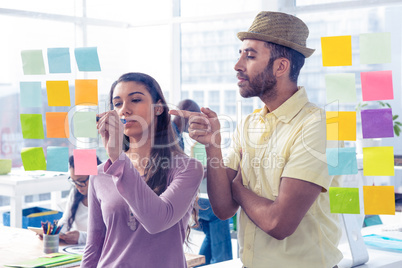 Businessman pointing while businesswoman writing on adhesive not