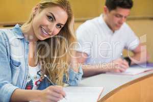 Smiling female student writing during class