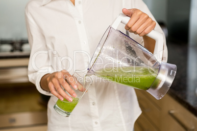 Mid section of woman pouring smoothie in a glass
