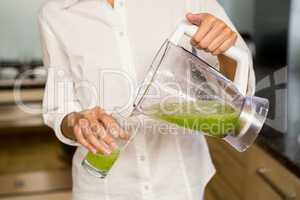 Mid section of woman pouring smoothie in a glass