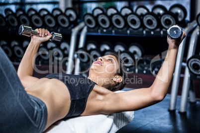 Muscular woman lifting dumbbell while sitting on bench